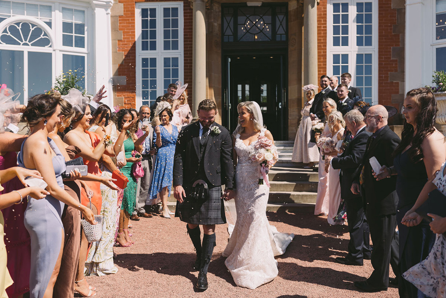 Guests throw confetti at couple as they walk through the crowd