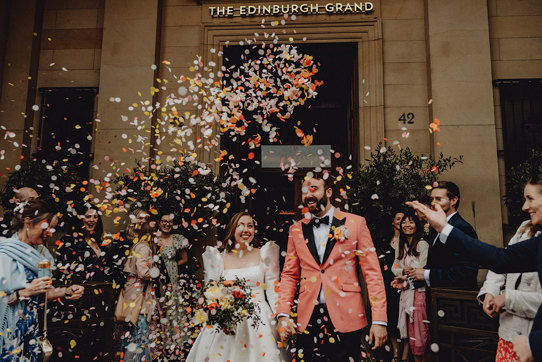 A bride and groom walking down the street with confetti falling.