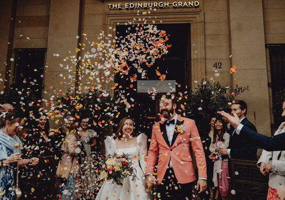 A bride and groom walking down the street with confetti falling.