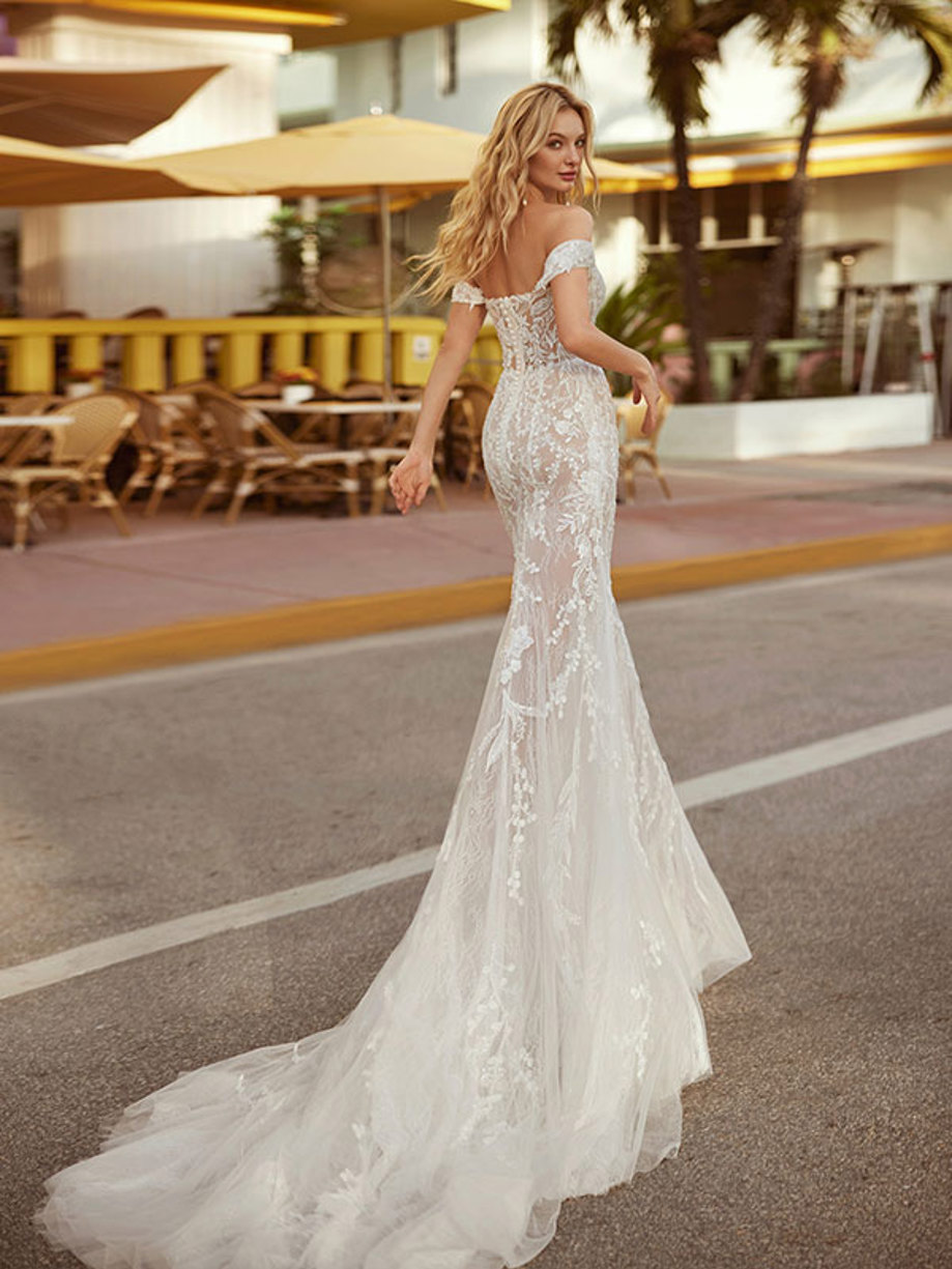 blonde woman wearing intricate applique white figure-hugging gown with off the shoulder sleeves