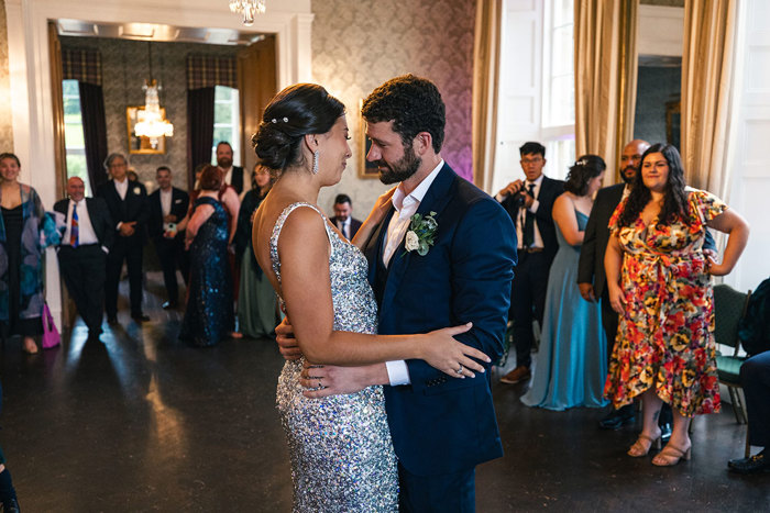 an emotional looking bride wearing silver and groom wearing dark blue suit dance at Blairquhan as surrounding wedding guests look on