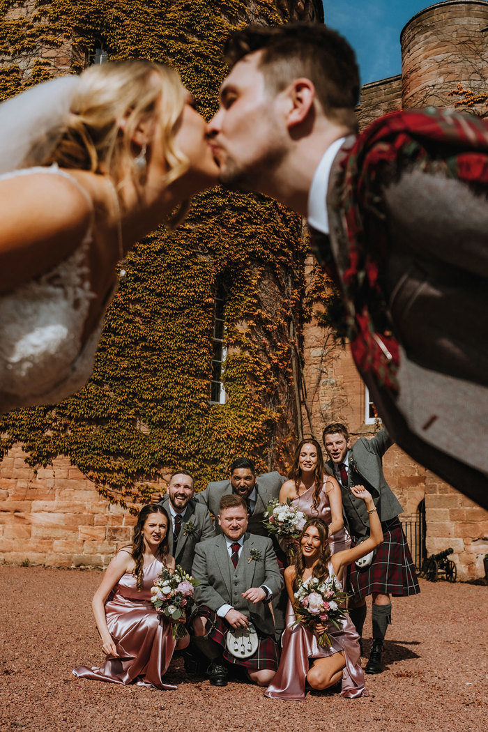 bride and groom kiss out of focus with wedding party in the background in focus