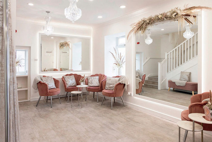 open airy room with dark pink velvet chairs and two large mirrors 