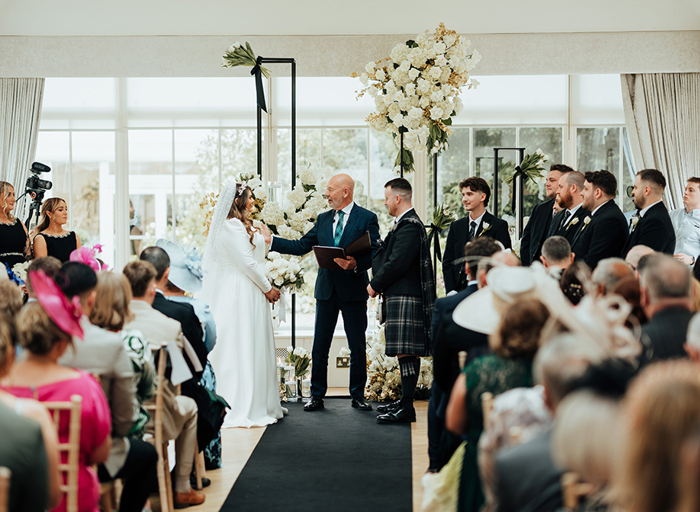 A wedding ceremony looking down the aisle at the bride and groom at the end with a celebrant standing in between them