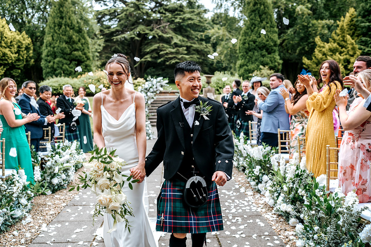wedding guests throw white confetti over bride and groom after outdoor ceremony at mar hall