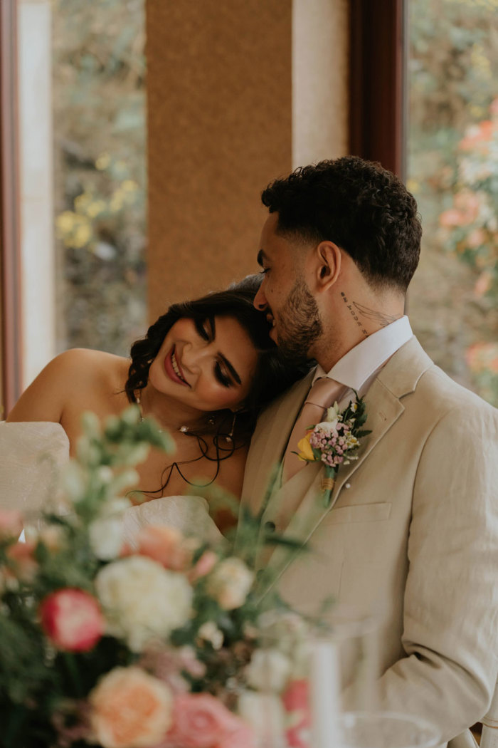 A bride leans her head on her husband's shoulder as they sit at the top table