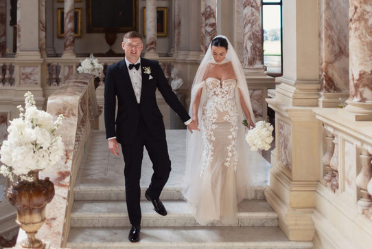 a bride wearing Berta Privee wedding dress and a groom wearing a black tuxedo. They are walking down a marble stone staircase at Gosford House.