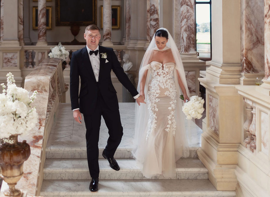 a bride wearing Berta Privee wedding dress and a groom wearing a black tuxedo. They are walking down a marble stone staircase at Gosford House.