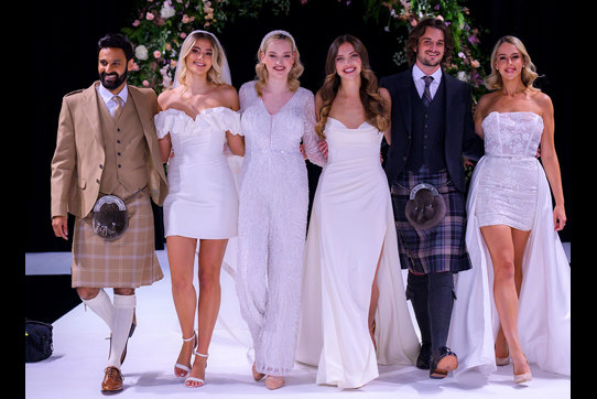 Group of men in kilts and women in wedding dresses standing next to each other 