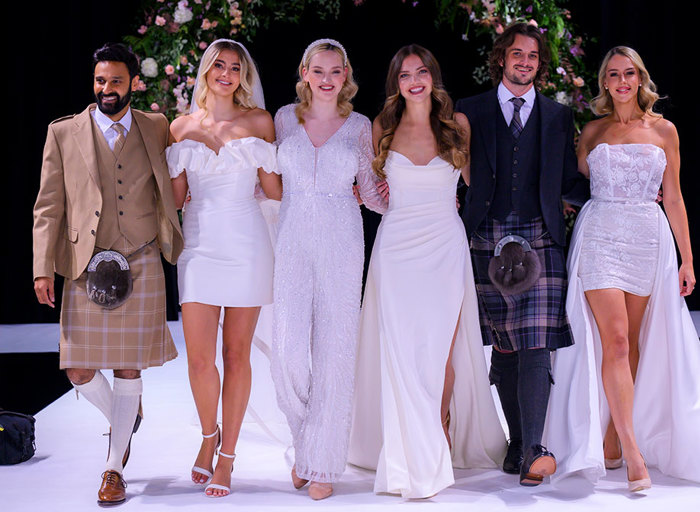 Group of men in kilts and women in wedding dresses standing next to each other 