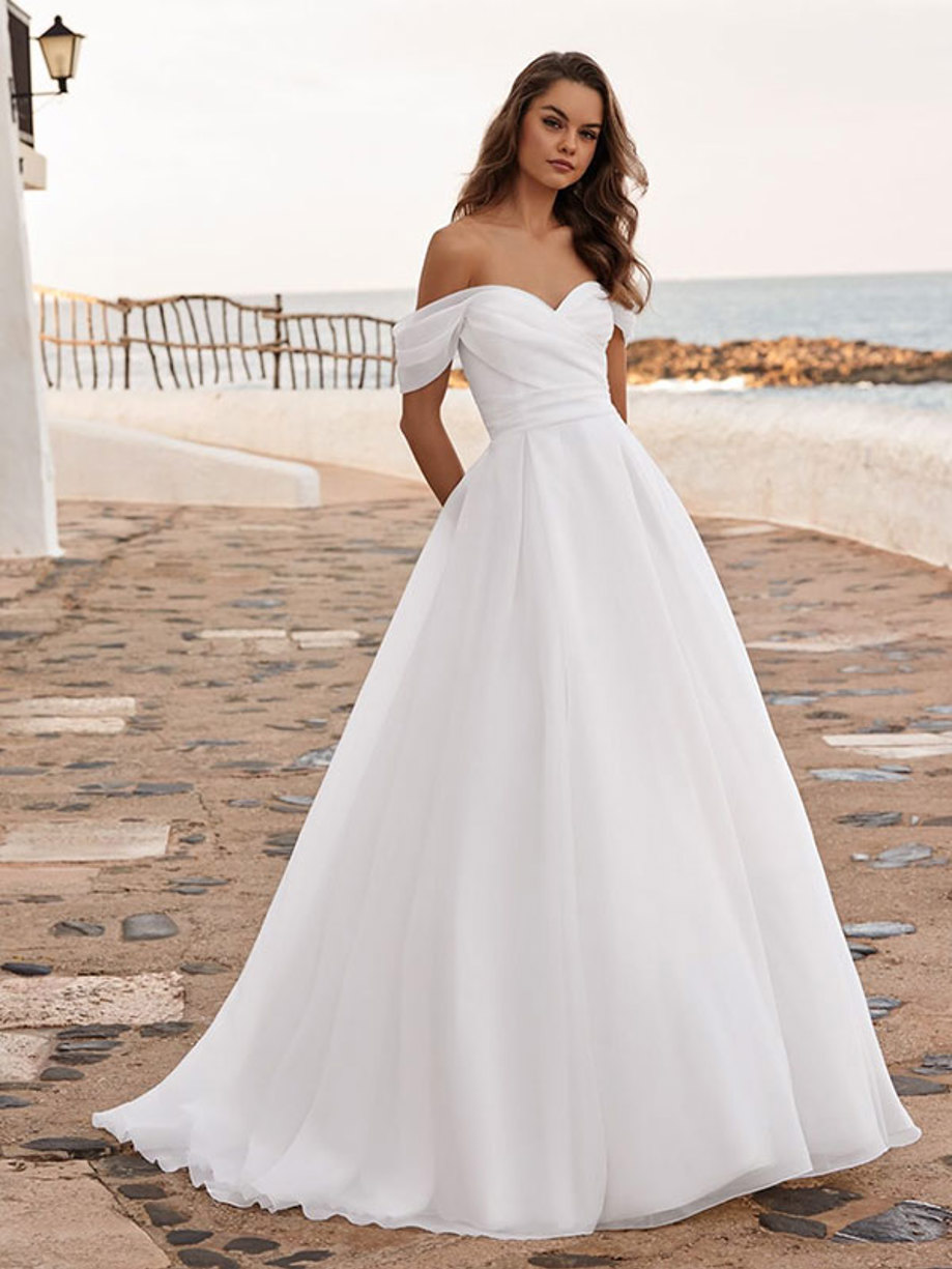 woman stands outdoors wearing an off-the-shoulder sweetheart neckline ballgown wedding dress