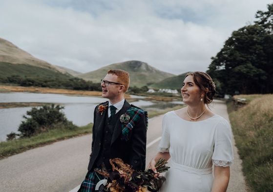 Couple walk on road beside scenic loch