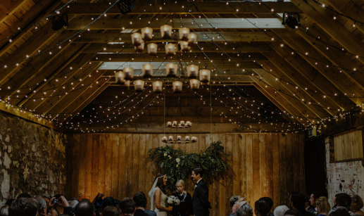 bride and groom stand in front of celebrant during an indoor wedding in ceremony room with wooden beams at byre at inchyra