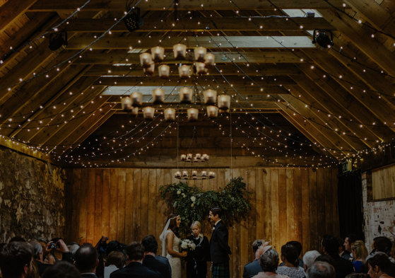 bride and groom stand in front of celebrant during an indoor wedding in ceremony room with wooden beams at byre at inchyra