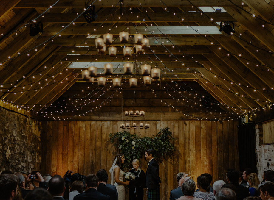bride and groom stand in front of celebrant during an indoor wedding in ceremony room with wooden beams at byre at inchyra