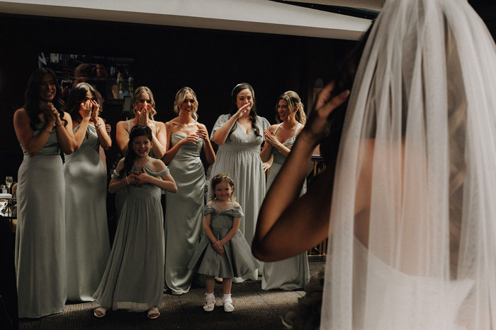 a row of women and children wearing pale green dresses looking on to a bride