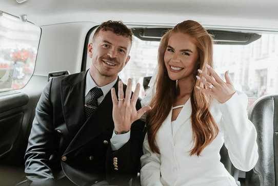 Man and woman sitting in a taxi holding their hands up to show off their wedding rings