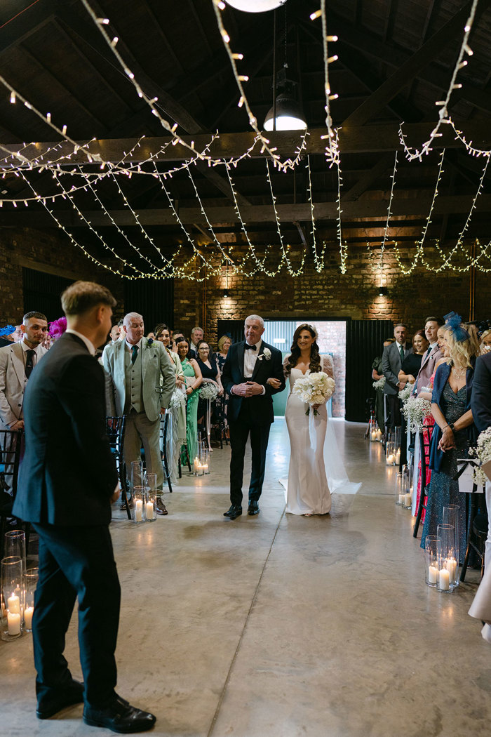 a bride walking down an aisle with a man in a smart black suit