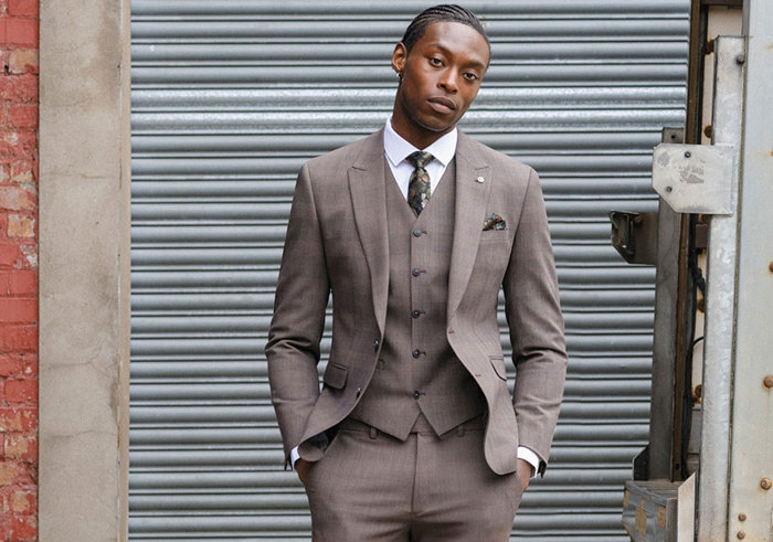 man standing with hands in trouser pockets wearing tailored light brown suit