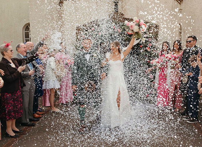 a white flurry of confetti with bride and groom walking through it and guests throwing confetti either side