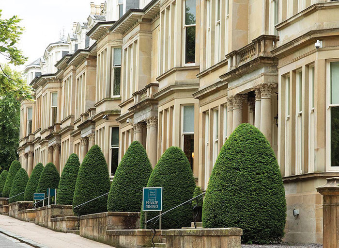 A blonde sandstone tenement building with neatly trimmed bushes outside the windows 