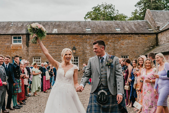 a bride and groom walking past their guests with the bride holding her bouquet high in the air