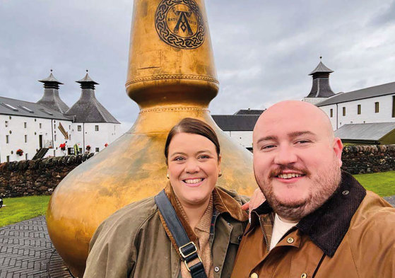 Two people standing in front of a large gold whisky still.