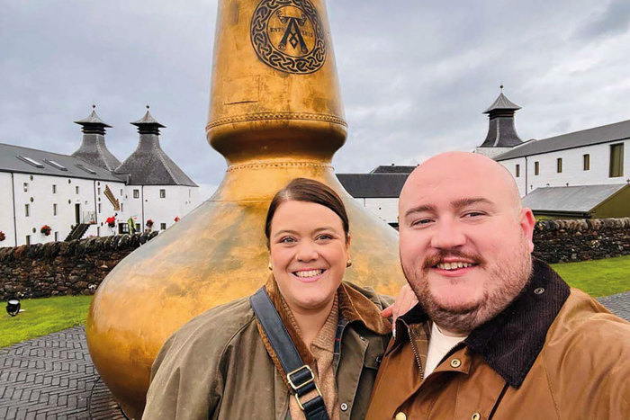 Two people standing in front of a large gold whisky still.