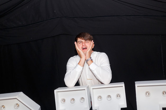 a man in a white shirt rests his face in his hands with his elbows on top of a giant light up letter