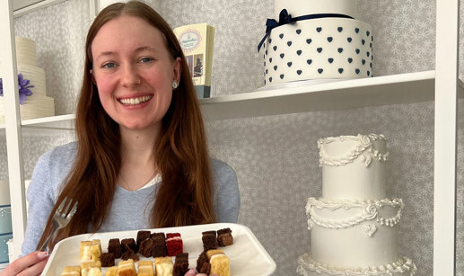 a brown haired woman stands in front of shelves with wedding cakes holding a tray of tiny different flavoured cake slices