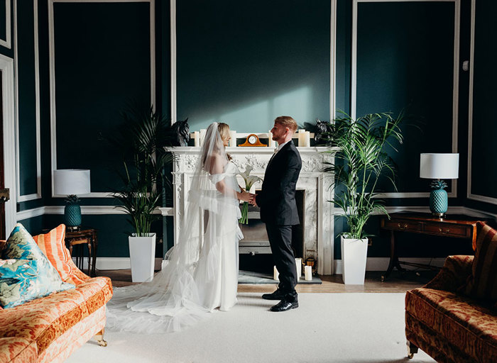 a bride and groom standing face to face in front of an ornate white fireplace at Elrick House