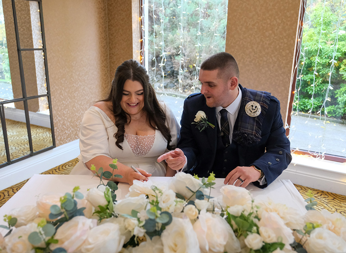 A bride and groom sign their marriage license at a white table covered in white roses 