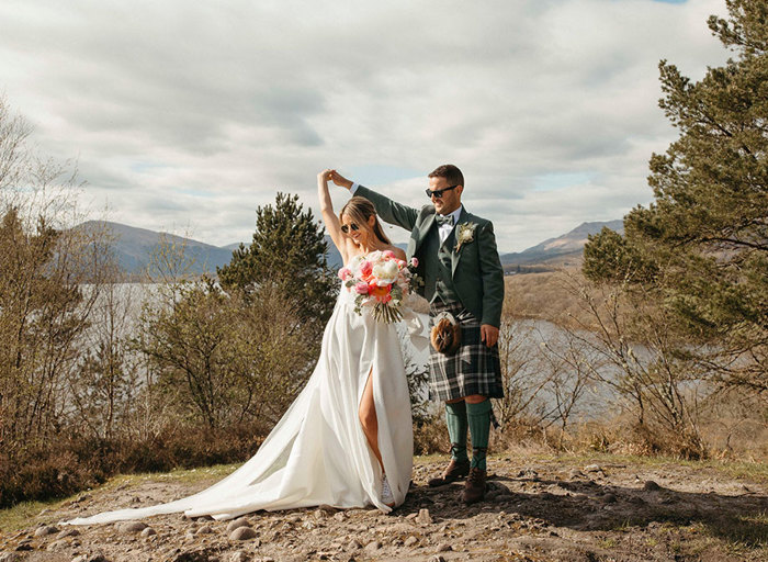 a bride and groom dancing on stony ground with beautiful landscape, trees and lake behind them