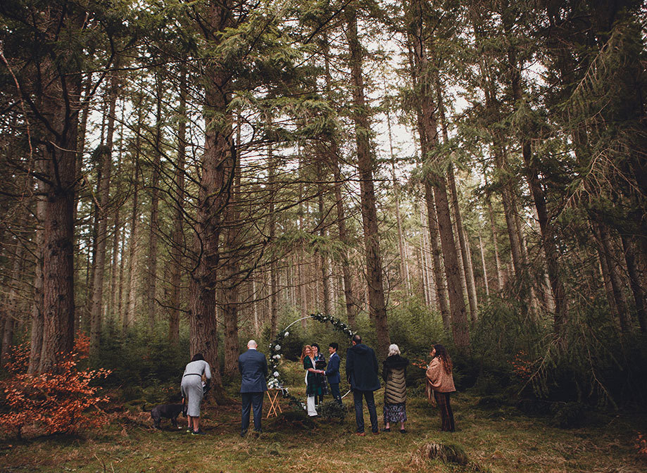 A small wedding ceremony in a forest with a moongate, two brides and five guests