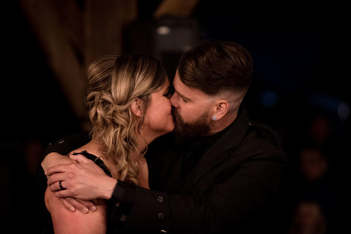 A Bride And Groom Wearing Black Embrace And Kiss