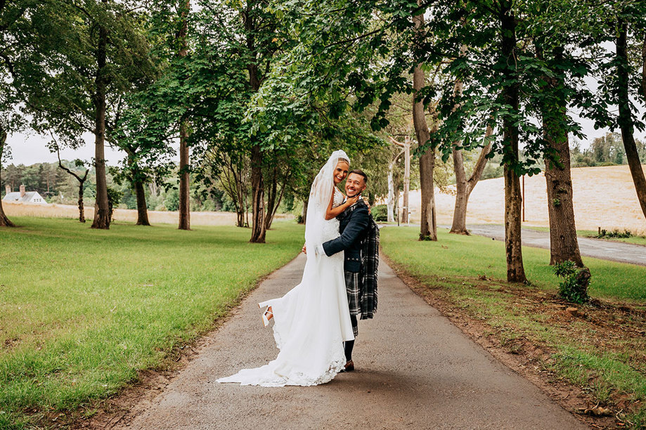 Groom lifts bride as they smile on path 