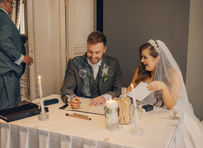 bride and groom sitting at table with candles signing register