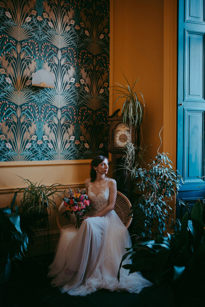 a bride sitting on a round wooden chair in a yellow and teal decorated room surrounded by potted plants at Netherbyres House