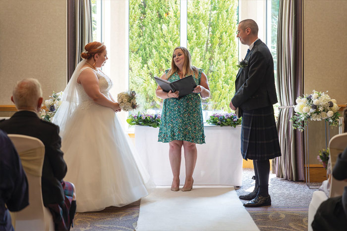 Bride and groom stand with their celebrant at top of the aisle