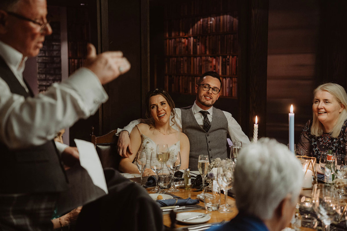 Bride and groom watch guest doing wedding speech