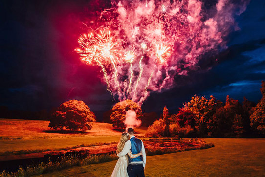 The newly-weds watch a red and purple display of fireworks go off in the night sky