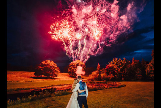 The newly-weds watch a red and purple display of fireworks go off in the night sky