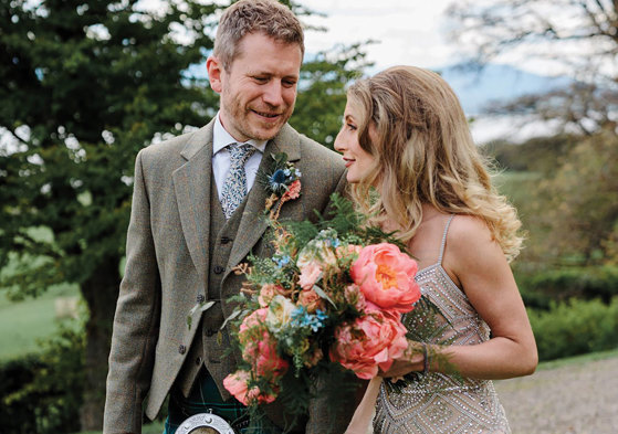 bride carries a colourful bouquet of flowers next to groom