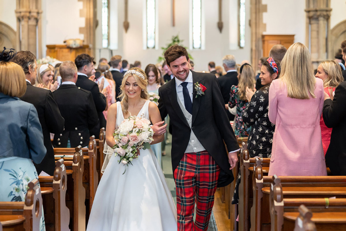 Couple walk up the aisle linking arms 