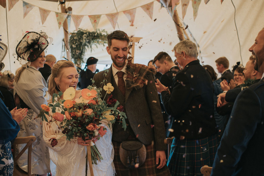 Guests throw confetti at couple as they walk through the crowd