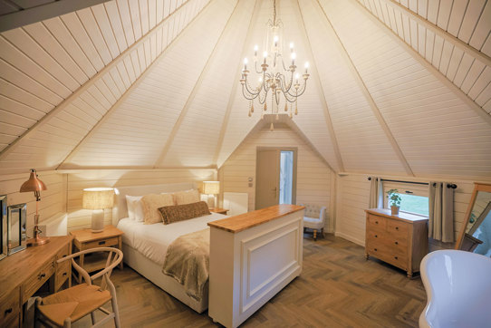 Spacious neutral coloured bedroom with chandelier hanging in centre