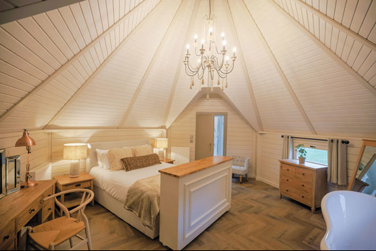 Spacious neutral coloured bedroom with chandelier hanging in centre