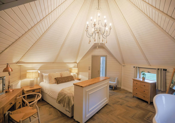 Spacious neutral coloured bedroom with chandelier hanging in centre