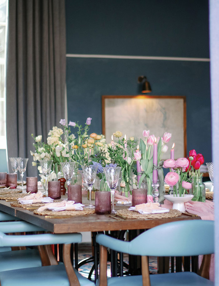 blue chairs are gathered around a long wooden table decorated with lots of florals, greenery, glassware and candle sticks