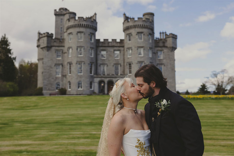 a bride and groom kissing in front of Cluny Castle.